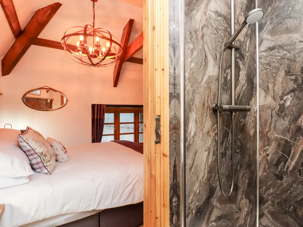 Cozy Bagtor Granary bedroom with exposed beams and a chandelier, next to a bathroom featuring a marble-style shower.