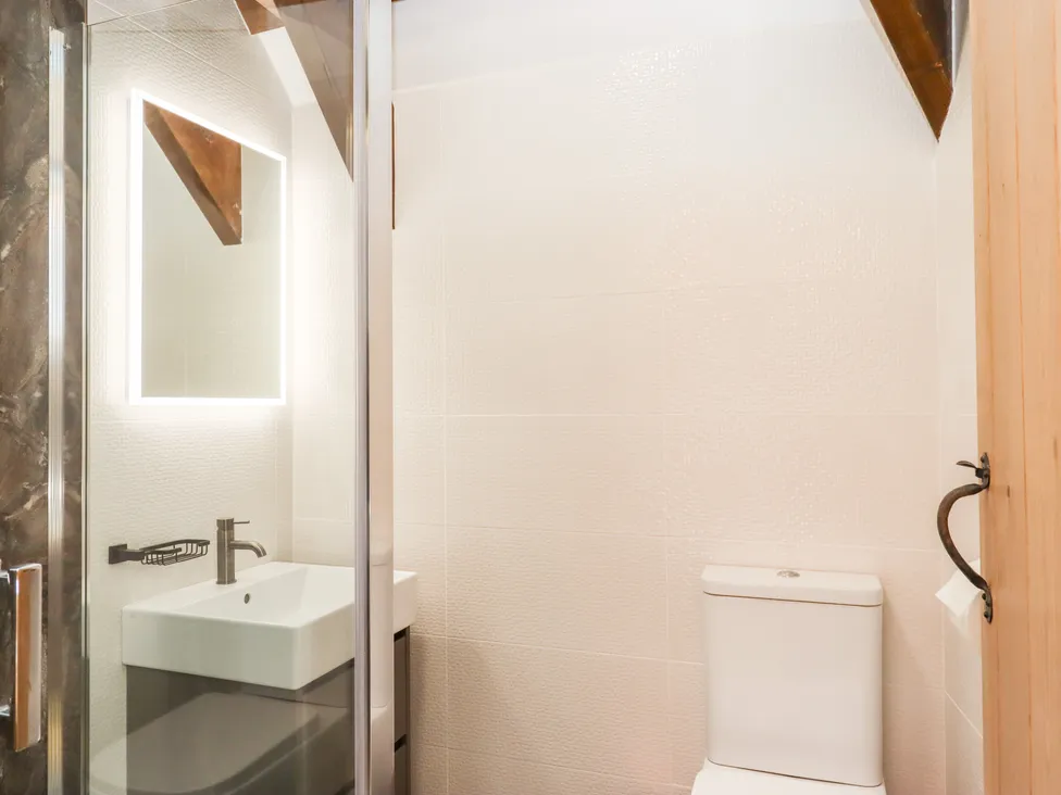 Modern bathroom with a white toilet, sink, and illuminated mirror, featuring wooden accents reminiscent of Bagtor Granary.