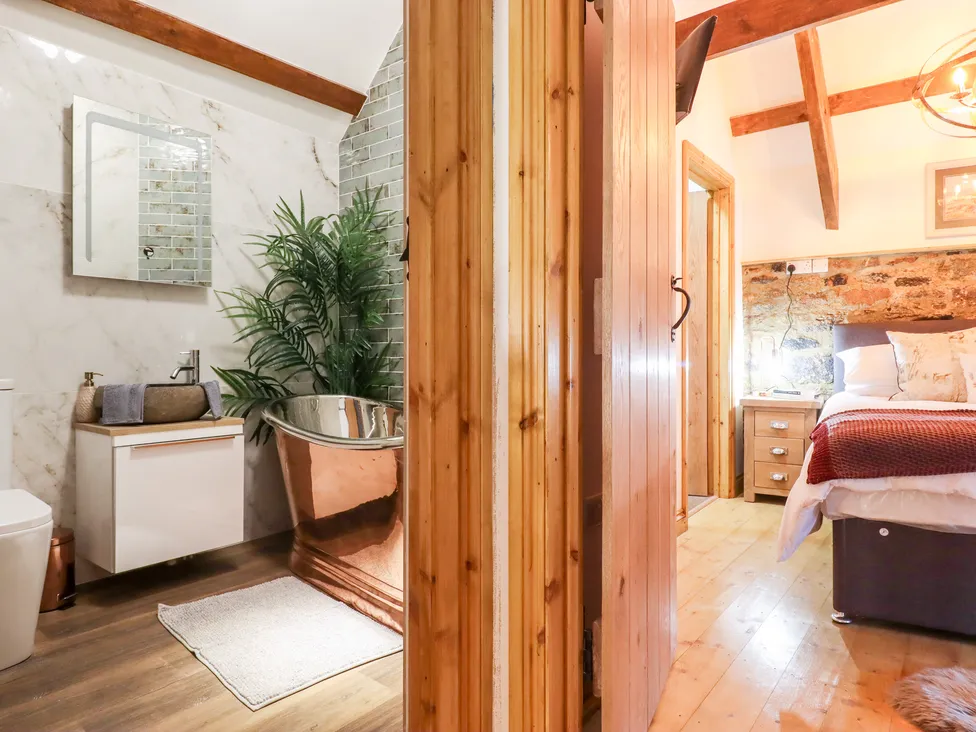 Cozy room at Bagtor Granary with a split view of modern bathroom and bedroom, featuring wood accents and warm lighting.