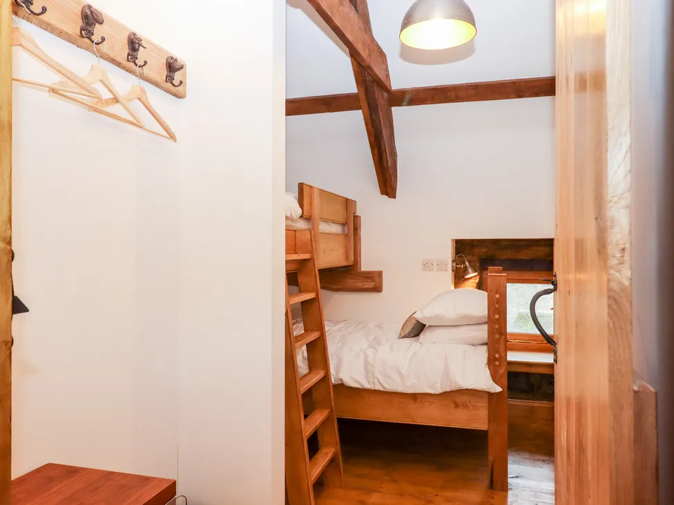 Cozy rustic bedroom in Bagtor Granary with wooden bunk beds, a small window, and exposed beams. Hangers adorn the wall.
