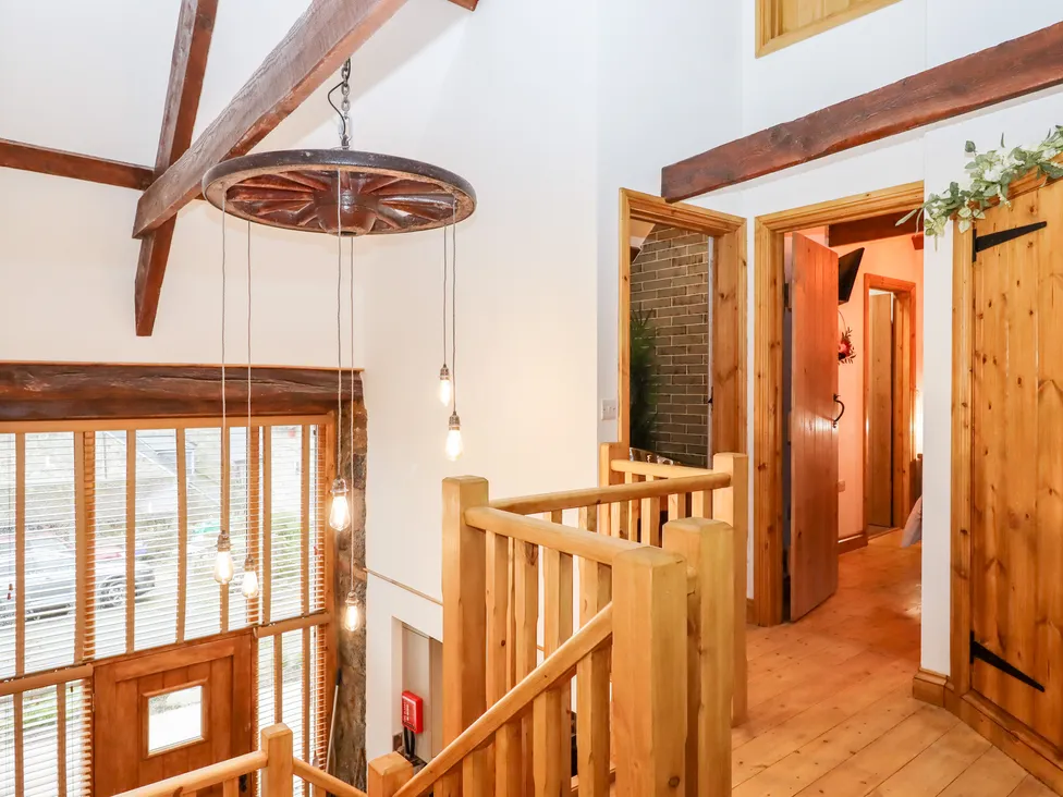Rustic Bagtor Granary interior with wooden beams, staircase, hanging lights, and a hallway with wooden doors. Bright natural light.