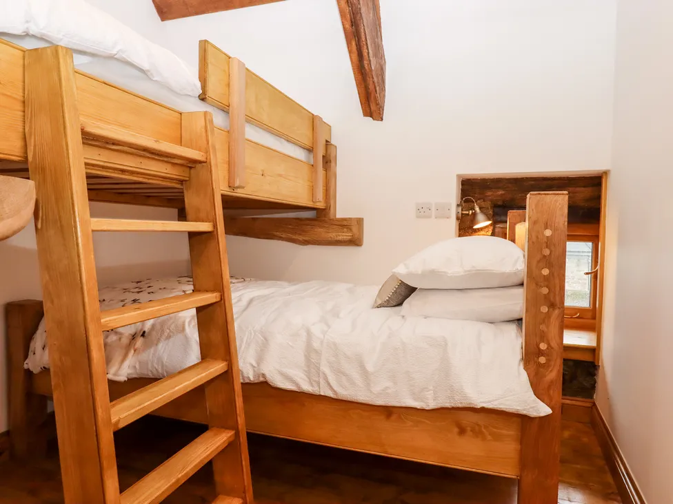 A wooden bunk bed in a cozy Bagtor room with white bedding, rustic beams, and a small bedside lamp.
