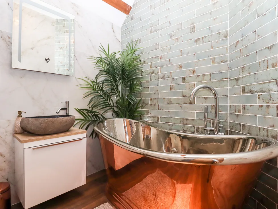 Modern bathroom with a copper bathtub, green tiled wall, marble sink, and Bagtor Granary charm beneath the mounted mirror.
