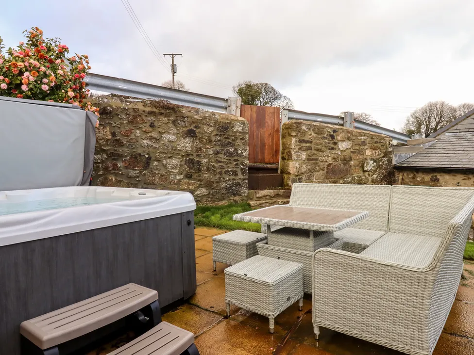 Patio with a hot tub and wicker furniture set, nestled by the stone walls of Bagtor Granary and lush plants.