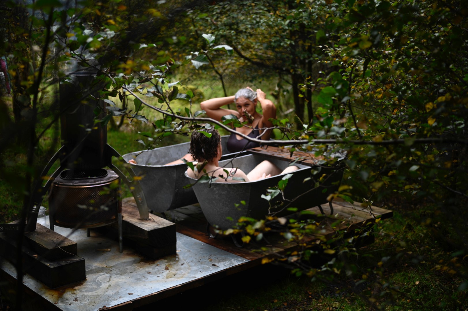 Two people relax in outdoor metal bathtubs surrounded by greenery, a peaceful moment captured by ToWander UK.