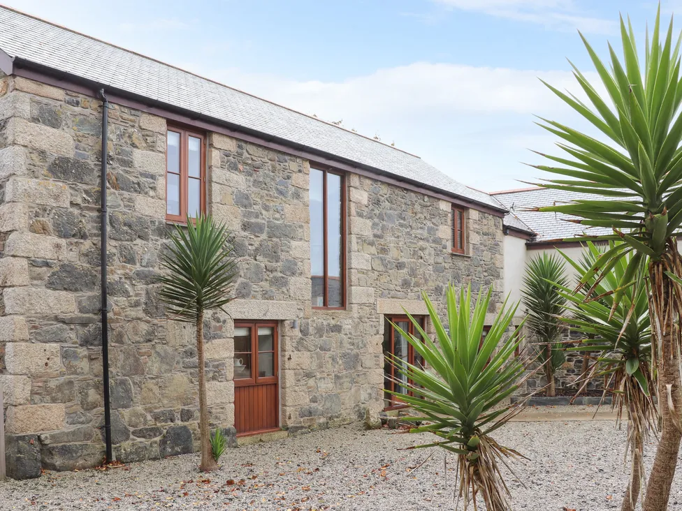 Pol Glas Hall: Stone barn-style building with wooden doors, windows, gravel surroundings, and palm-like plants.