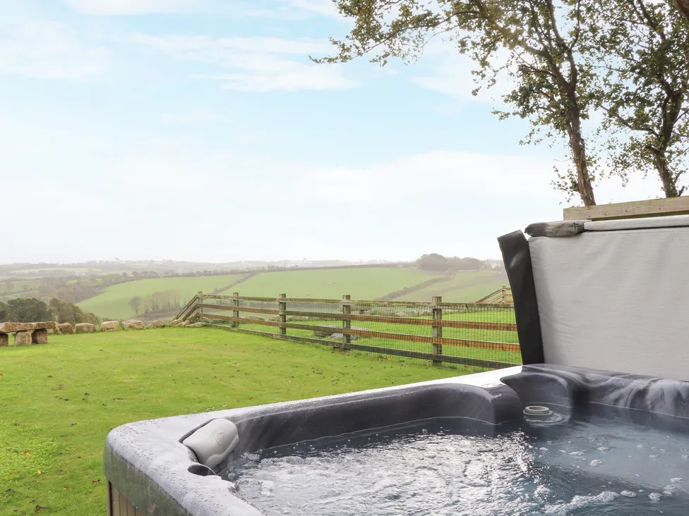 A bubbling hot tub at Pol Glas Hall overlooks a grassy field and rolling green hills under a bright sky.