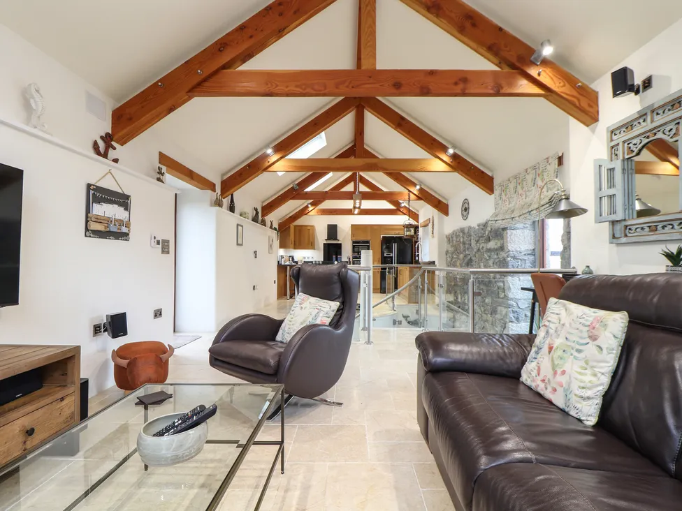 Modern loft living space with exposed wooden beams, leather seating, and a Pol Glas Hall-inspired glass coffee table.