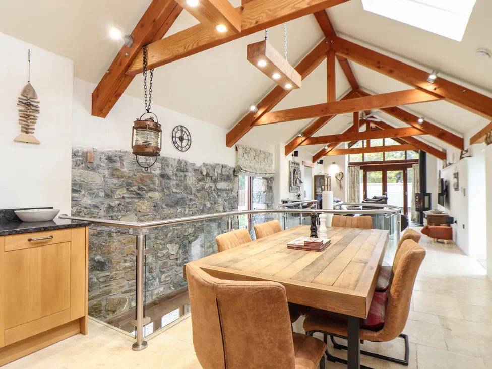Dining area in Pol Glas Hall with wooden table, cushioned chairs, stone wall, exposed beams, and skylights.