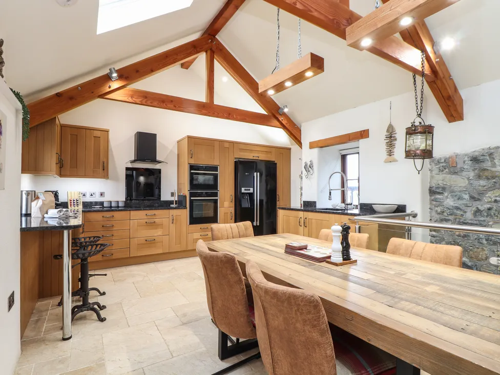 Modern rustic kitchen with wooden beams, stone wall, and wood cabinets inspired by Pol Glas Hall’s timeless charm.