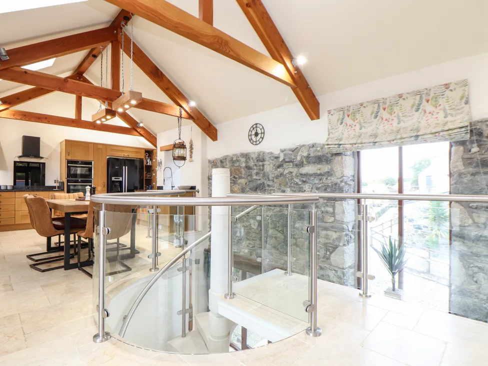 Kitchen with wooden beams, stone wall, and Pol Glas Hall–inspired spiral glass staircase, bathed in natural light.