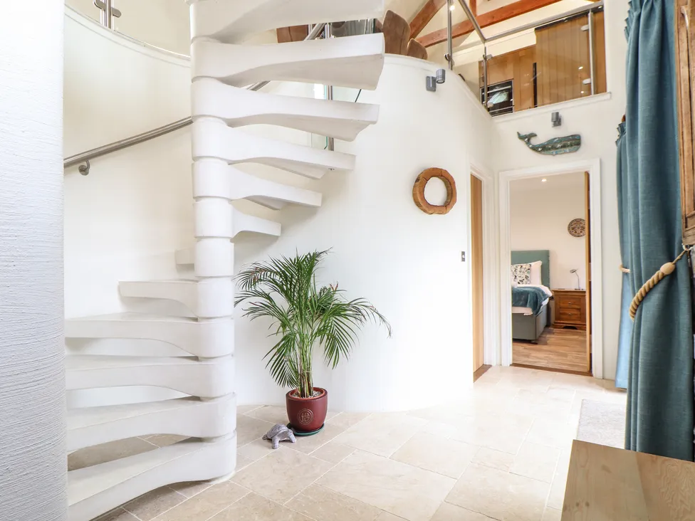 White spiral staircase in Pol Glas Hall with a potted plant below, leading to a bright bedroom in a modern home.