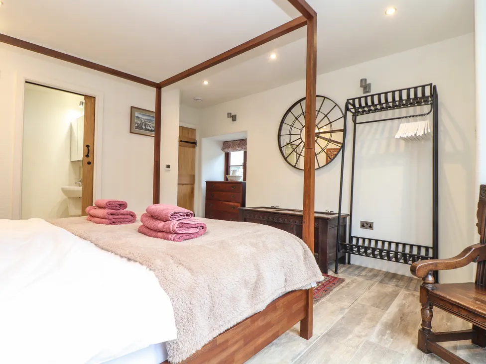 A cozy bedroom at Pol Glas Hall with a canopy bed, pink towels, wall mirror, and wooden chair on a wooden floor.
