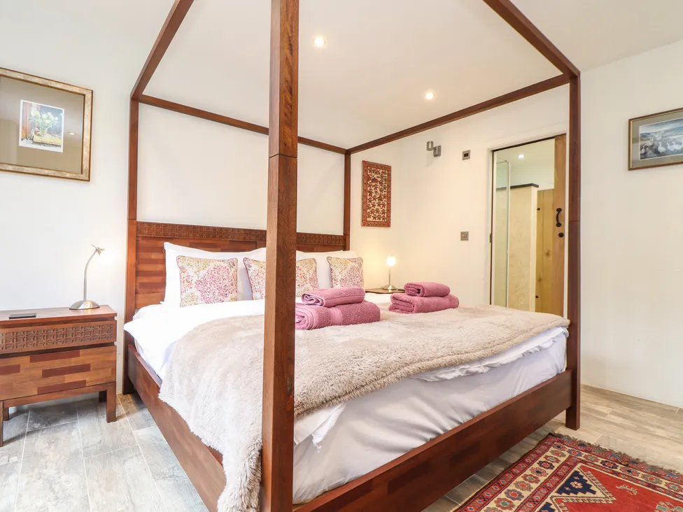 A cozy bedroom at Pol Glas Hall with a wooden four-poster bed, pink towels, and patterned pillows on a fluffy blanket.