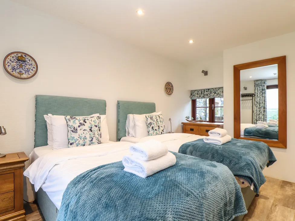 Bright bedroom at Pol Glas Hall with two twin beds, teal blankets, floral pillows, and folded towels.