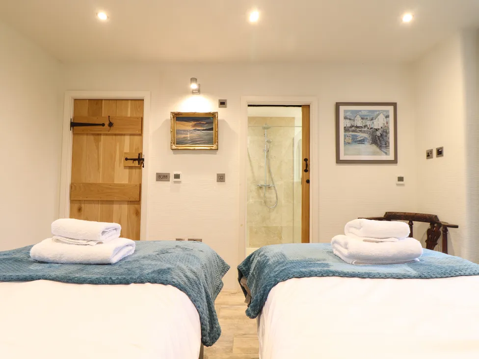 Two beds with folded towels in a bright, modern Pol Glas Hall room with art and a view of the shower.