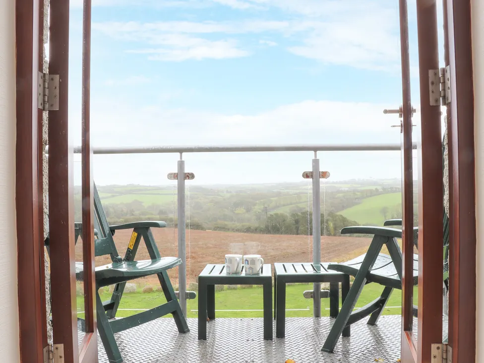 Two chairs and a table with cups on a balcony at Pol Glas Hall, overlooking green hills under a blue sky.