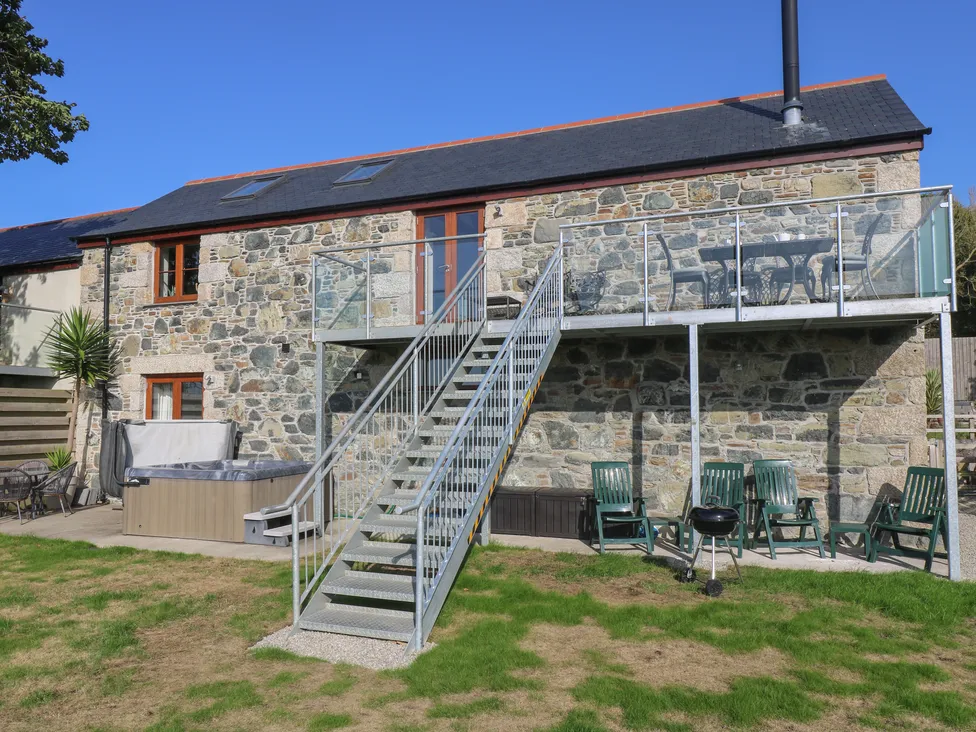 Pol Glas Hall: Stone house with metal staircase, balcony, green chairs, hot tub, and grill on a grassy lawn.