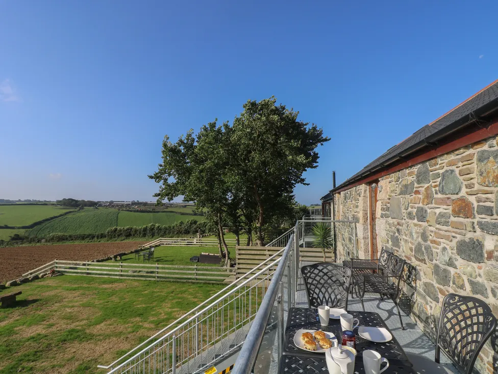 Breakfast on a balcony overlooking green fields, trees, and Pol Glas Hall under a clear blue sky.